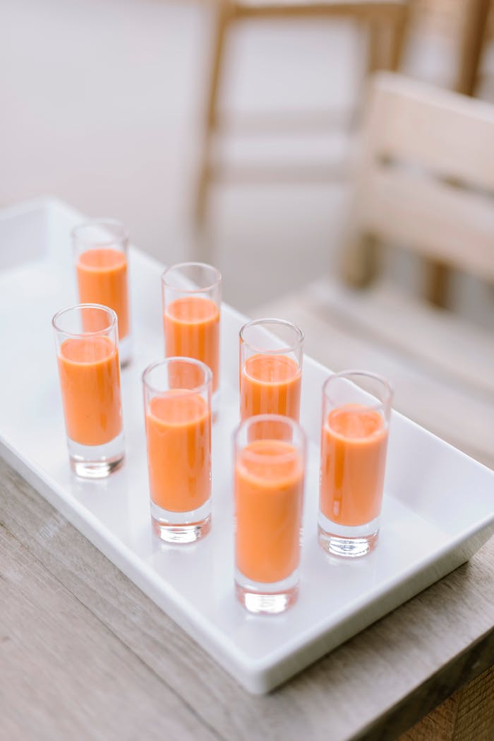 who-we-are Aesthetic display of orange smoothie shots on a white tray, ideal for parties.